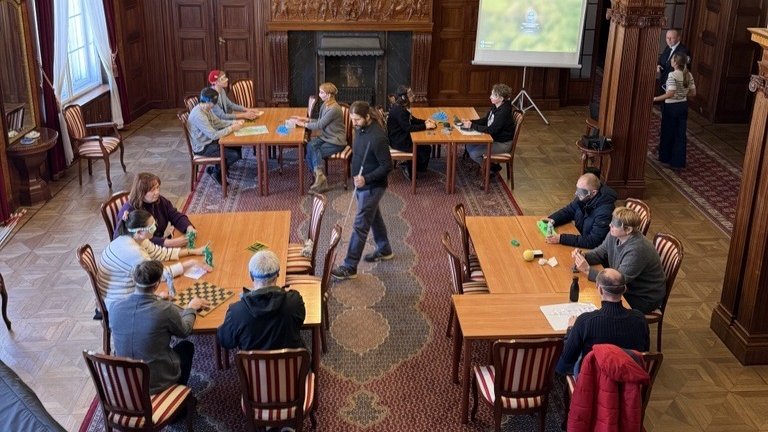 A group of blindfolded people sitting at tables in a room of the Biedermann's Palace